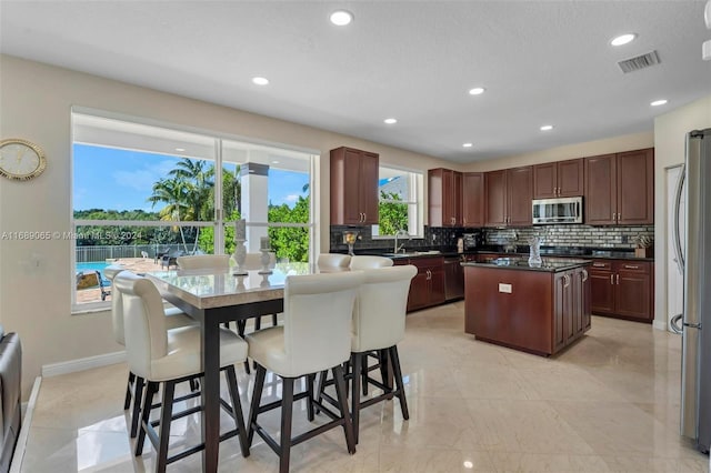 kitchen featuring sink, a textured ceiling, appliances with stainless steel finishes, tasteful backsplash, and a kitchen island