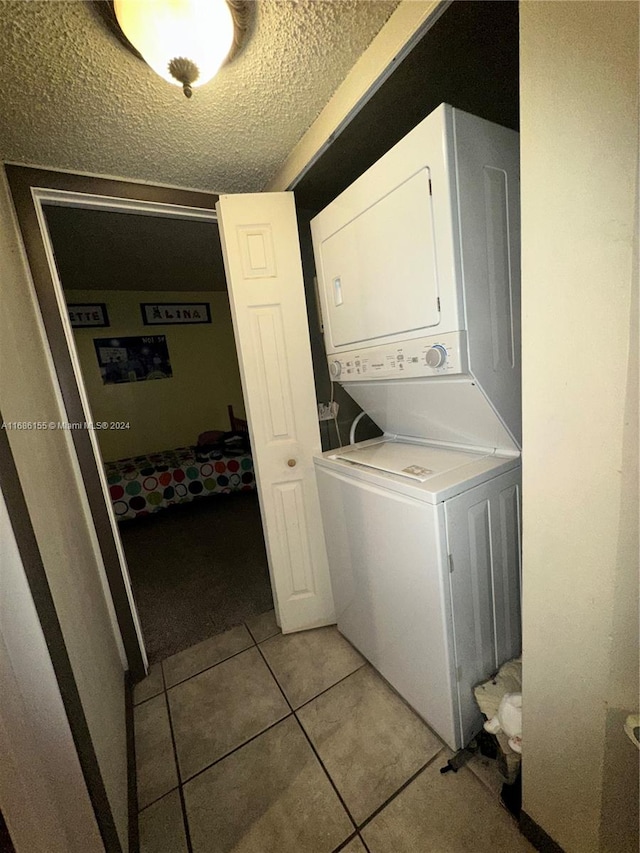 washroom featuring a textured ceiling, light tile patterned floors, and stacked washer / drying machine