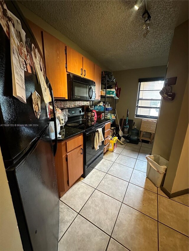 kitchen with a textured ceiling, light tile patterned floors, black appliances, and tasteful backsplash