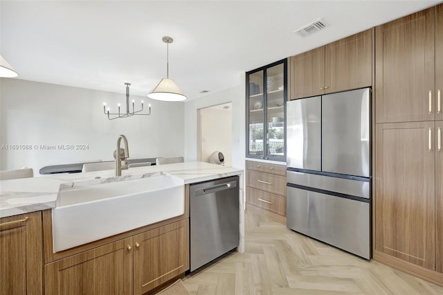 kitchen featuring stainless steel appliances, light stone counters, light parquet floors, sink, and pendant lighting