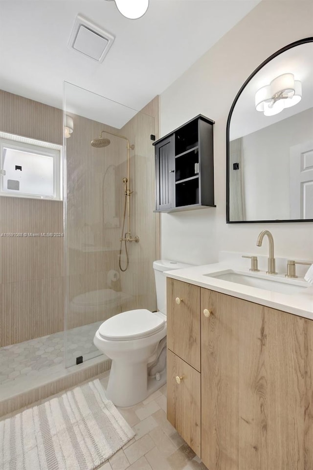 bathroom with toilet, vanity, tile patterned floors, and tiled shower