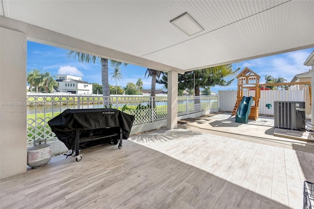 wooden deck featuring central AC unit, a playground, a water view, and a grill