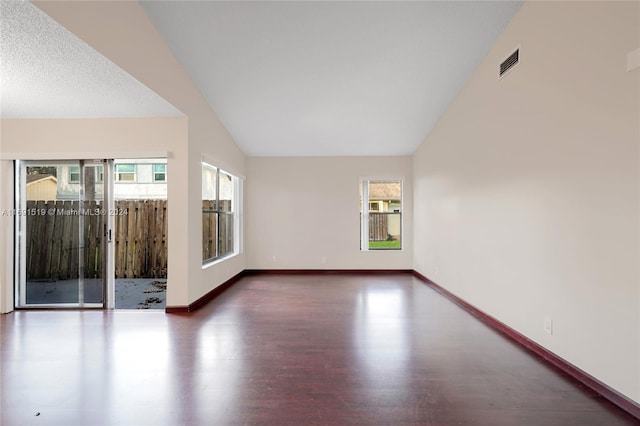 spare room with dark hardwood / wood-style flooring, a textured ceiling, and vaulted ceiling