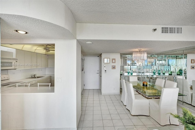 unfurnished dining area featuring sink, a textured ceiling, light tile patterned flooring, and ceiling fan with notable chandelier