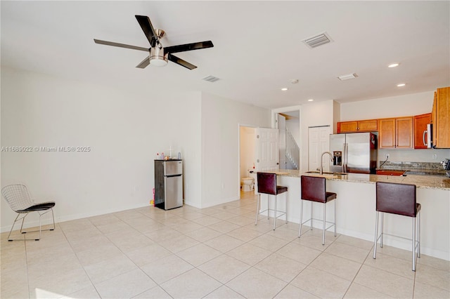 kitchen with sink, a breakfast bar area, ceiling fan, light stone countertops, and stainless steel appliances