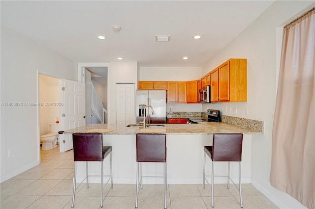 kitchen with sink, stainless steel appliances, light stone counters, kitchen peninsula, and a kitchen bar