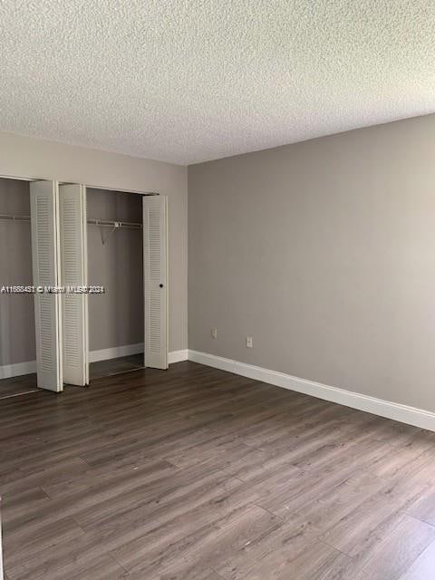 unfurnished bedroom with two closets, a textured ceiling, and dark hardwood / wood-style flooring