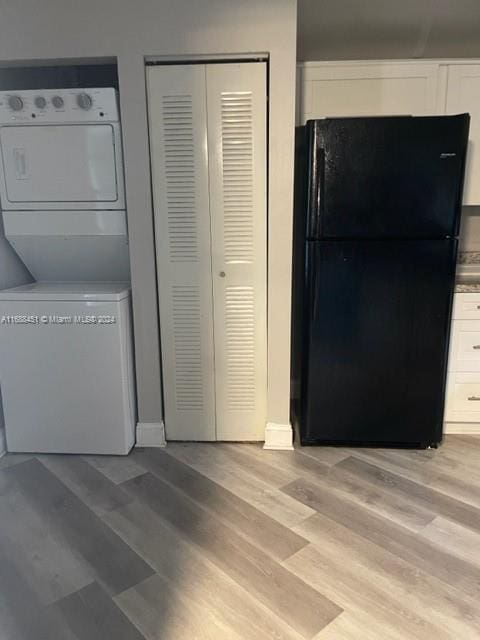 kitchen with white cabinets, stacked washer and dryer, black refrigerator, and light wood-type flooring