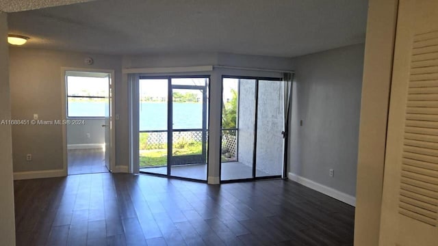 empty room with a water view, a textured ceiling, and dark hardwood / wood-style floors