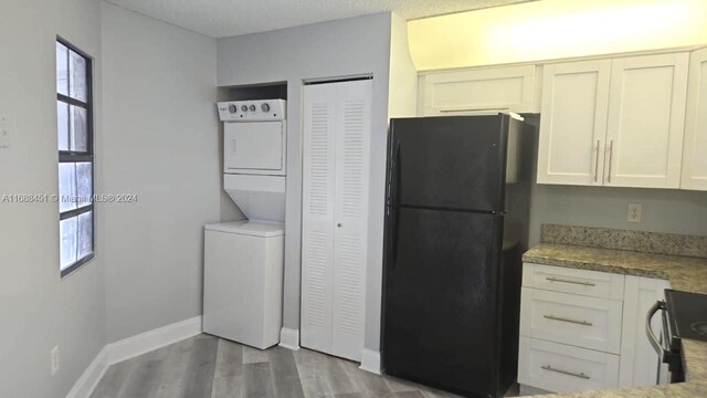 kitchen with white cabinetry, light hardwood / wood-style floors, stacked washer / dryer, and black refrigerator