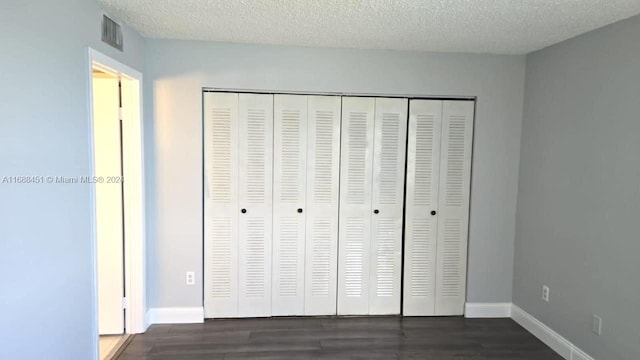 unfurnished bedroom featuring dark wood-type flooring, a textured ceiling, and a closet