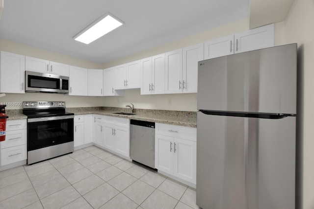 kitchen featuring light tile patterned flooring, white cabinetry, appliances with stainless steel finishes, light stone countertops, and sink