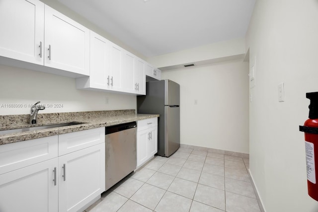 kitchen featuring stainless steel appliances, light stone counters, sink, light tile patterned floors, and white cabinetry