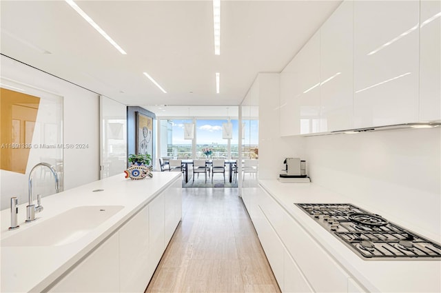 interior space featuring light hardwood / wood-style floors, white cabinetry, sink, floor to ceiling windows, and stainless steel gas stovetop