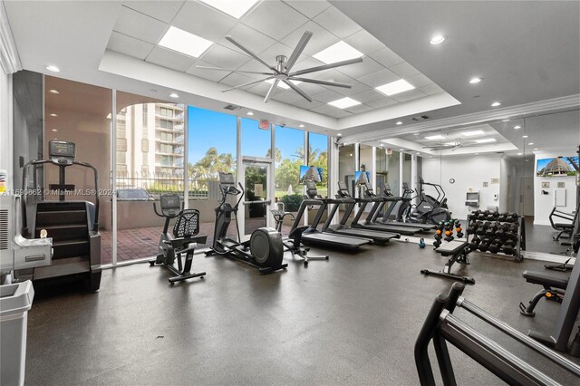 exercise room with a drop ceiling, ceiling fan, and a raised ceiling