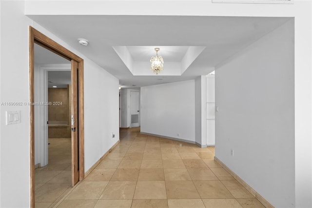 corridor with a notable chandelier, light tile patterned floors, and a raised ceiling