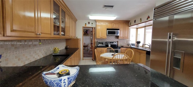 kitchen with sink, light tile patterned floors, dark stone counters, stainless steel appliances, and decorative backsplash