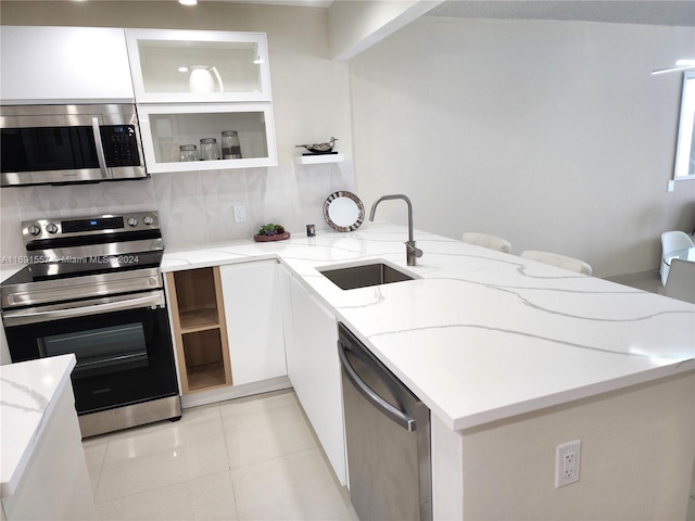 kitchen with white cabinetry, sink, kitchen peninsula, appliances with stainless steel finishes, and light stone countertops