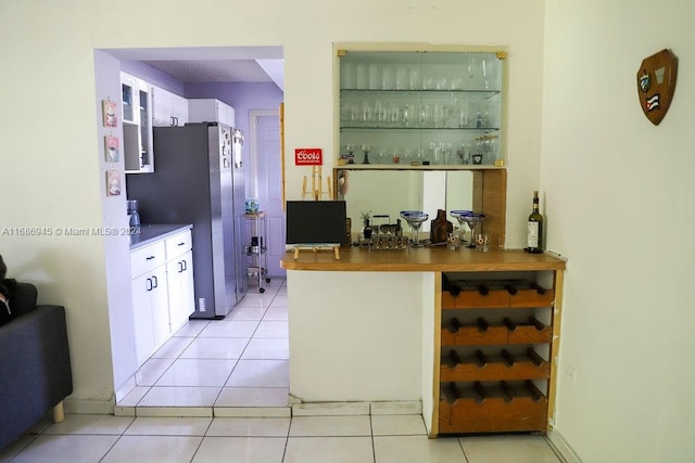 bar featuring stainless steel fridge, white cabinetry, and light tile patterned floors