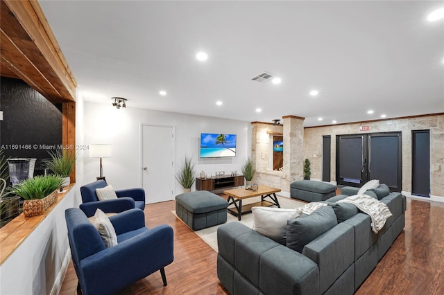 living room featuring wood-type flooring, crown molding, and ornate columns