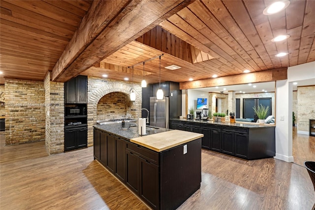 kitchen with stainless steel refrigerator, wooden ceiling, hanging light fixtures, light hardwood / wood-style floors, and a kitchen island with sink