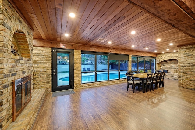 unfurnished dining area with a fireplace, hardwood / wood-style floors, wooden ceiling, and brick wall