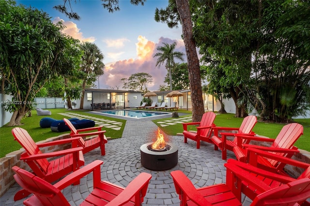 patio terrace at dusk with a fire pit, a fenced in pool, and a yard