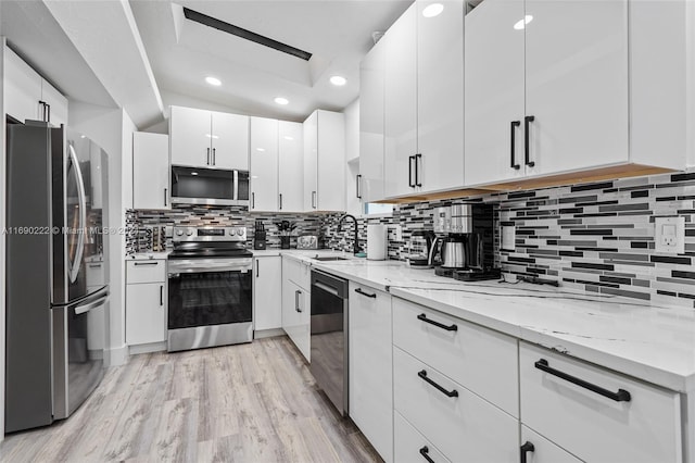 kitchen featuring tasteful backsplash, stainless steel appliances, light wood-type flooring, sink, and white cabinets