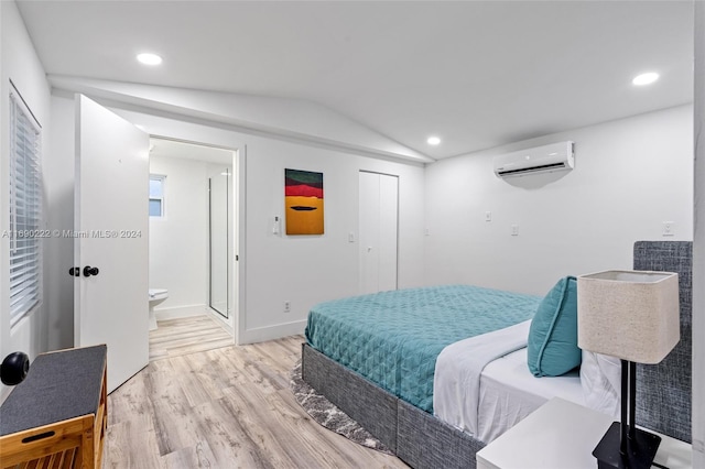 bedroom with light hardwood / wood-style floors, lofted ceiling, a wall mounted AC, and ensuite bath