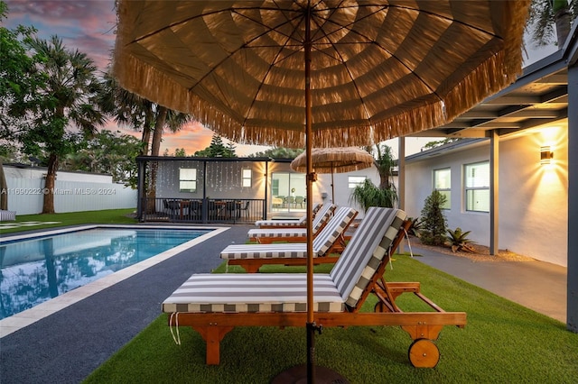 pool at dusk featuring a lawn and a patio