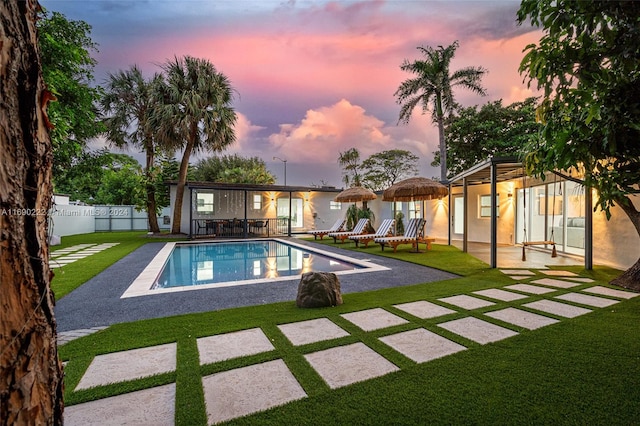 pool at dusk featuring a yard and a patio