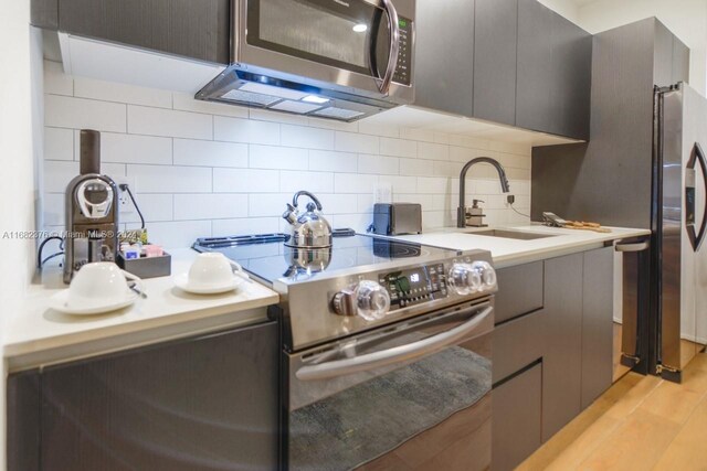 kitchen featuring stainless steel appliances, decorative backsplash, sink, gray cabinets, and light wood-type flooring