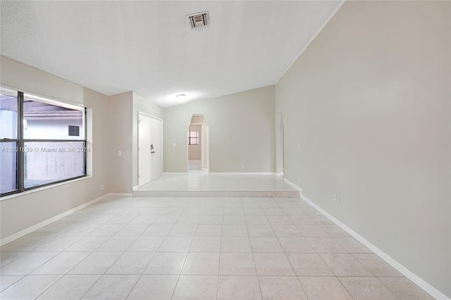 tiled spare room with a textured ceiling and vaulted ceiling