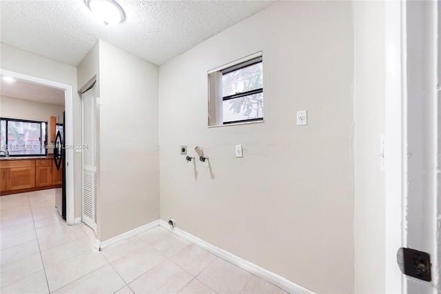 washroom with hookup for an electric dryer, washer hookup, a textured ceiling, and light tile patterned flooring