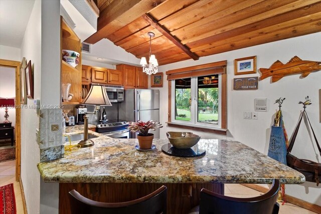 13470 SW 67th Ave, Pinecrest, FL 33156 - kitchen with appliances with stainless steel finishes, brown cabinetry, light stone counters, a peninsula, and a chandelier