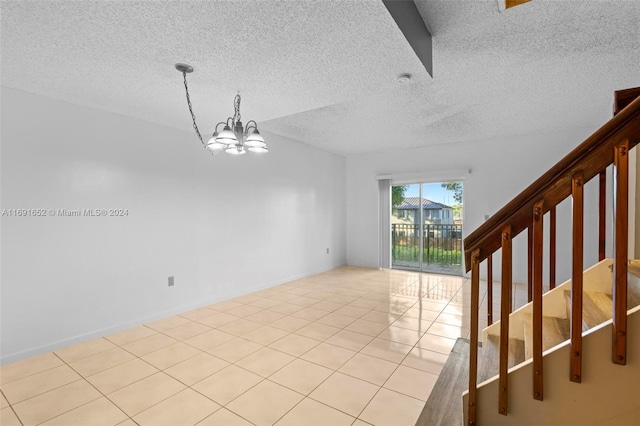 tiled spare room with a textured ceiling and a chandelier