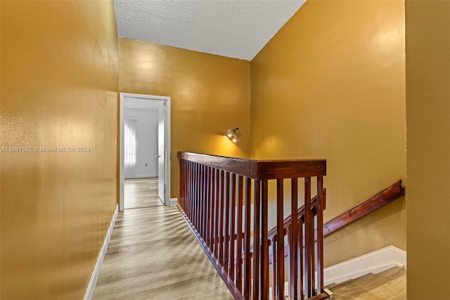 hall with hardwood / wood-style floors, a textured ceiling, and lofted ceiling