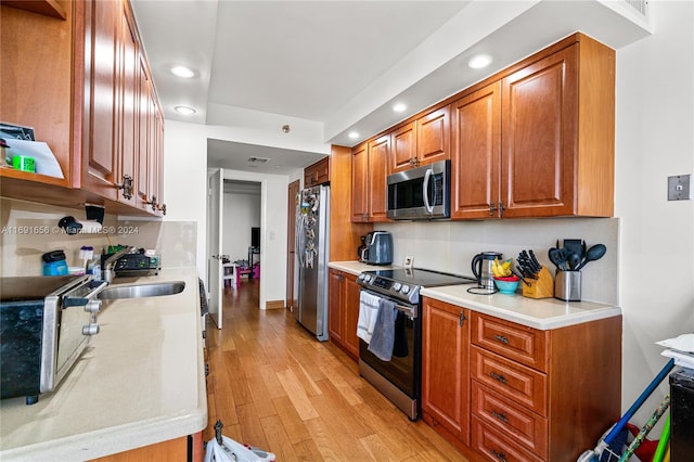 kitchen with decorative backsplash, sink, light wood-type flooring, and appliances with stainless steel finishes