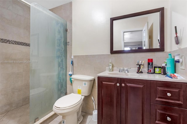 bathroom with tile patterned flooring, vanity, tile walls, toilet, and a tile shower