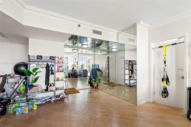 gym featuring hardwood / wood-style floors, crown molding, and a textured ceiling