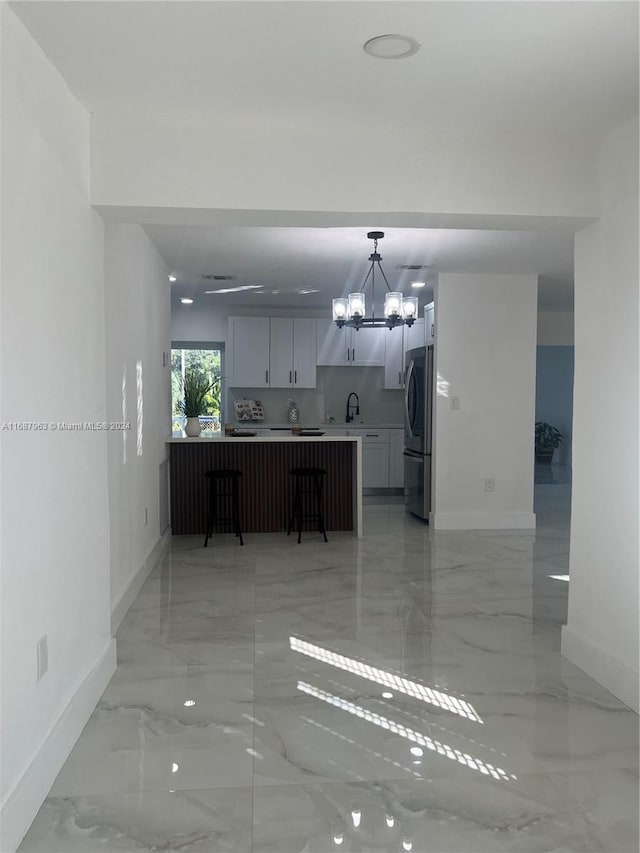 kitchen featuring stainless steel refrigerator, hanging light fixtures, sink, an inviting chandelier, and white cabinets