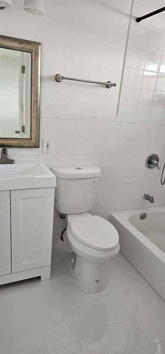 full bathroom featuring tile walls, vanity, tiled shower / bath combo, and toilet