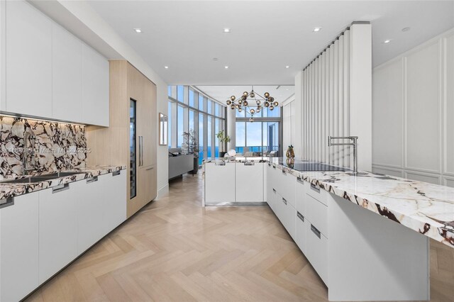 kitchen featuring white cabinets, a chandelier, light stone countertops, and light parquet floors