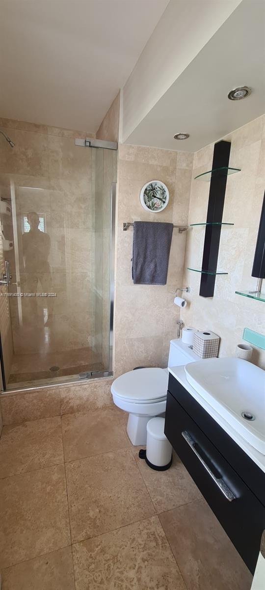 bathroom featuring walk in shower, vanity, toilet, and tile walls