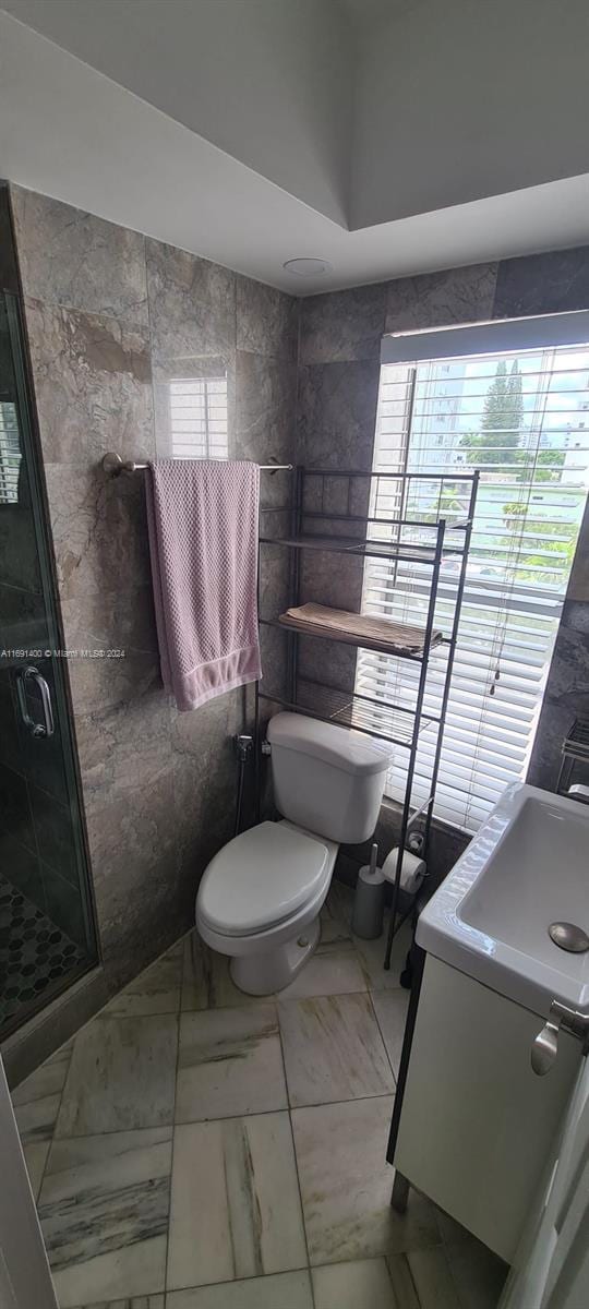 bathroom featuring toilet, a shower with door, and tile walls