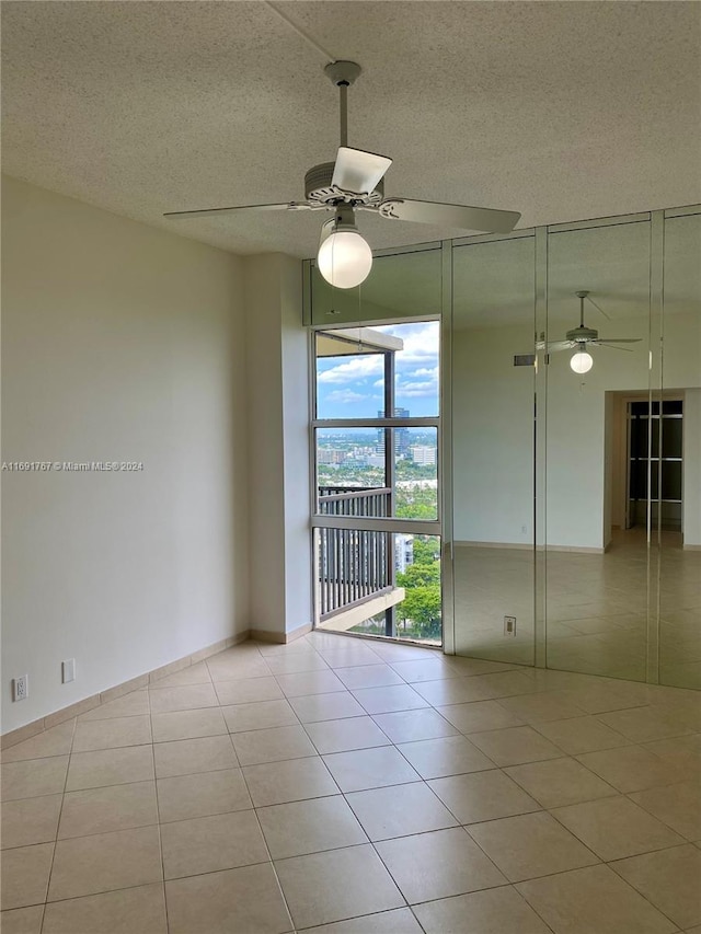 empty room featuring ceiling fan, expansive windows, light tile patterned floors, and a textured ceiling