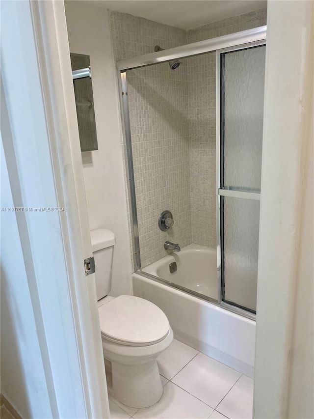 bathroom with combined bath / shower with glass door, tile patterned floors, and toilet