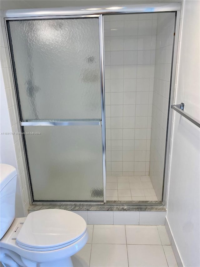 bathroom featuring tile patterned floors, toilet, and a shower with door