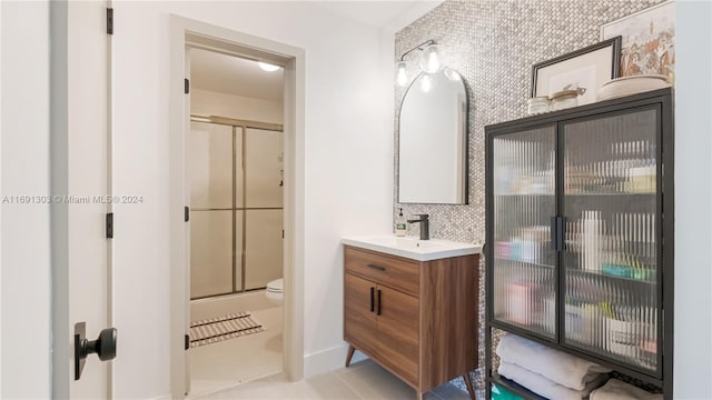 bathroom with a shower with door, vanity, toilet, and tile patterned flooring