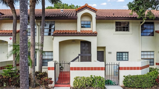 mediterranean / spanish home featuring a fenced front yard, a gate, a tiled roof, and stucco siding